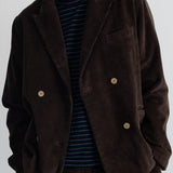 A person wearing a dark brown corduroy blazer over a navy and blue striped shirt, paired with matching corduroy trousers, against a plain light gray background.