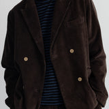 A person wearing a dark brown corduroy blazer over a navy and blue striped shirt, paired with matching corduroy trousers, against a plain light gray background.