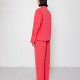 Person wearing a coral suit standing against a white wall.