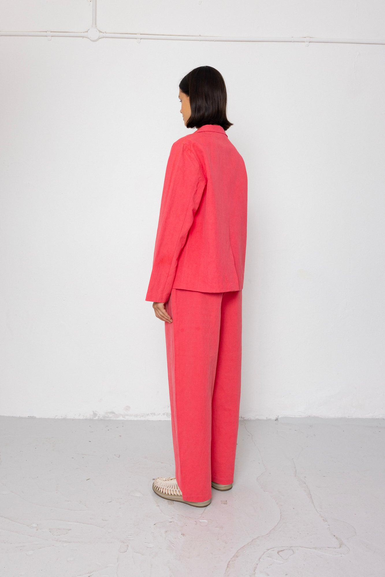 Person wearing a coral suit standing against a white wall.