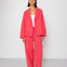 Woman wearing a coral suit standing against a white background