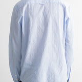 A person shown from the back wearing a light blue textured long-sleeve button-up shirt and dark trousers against a plain white background.
