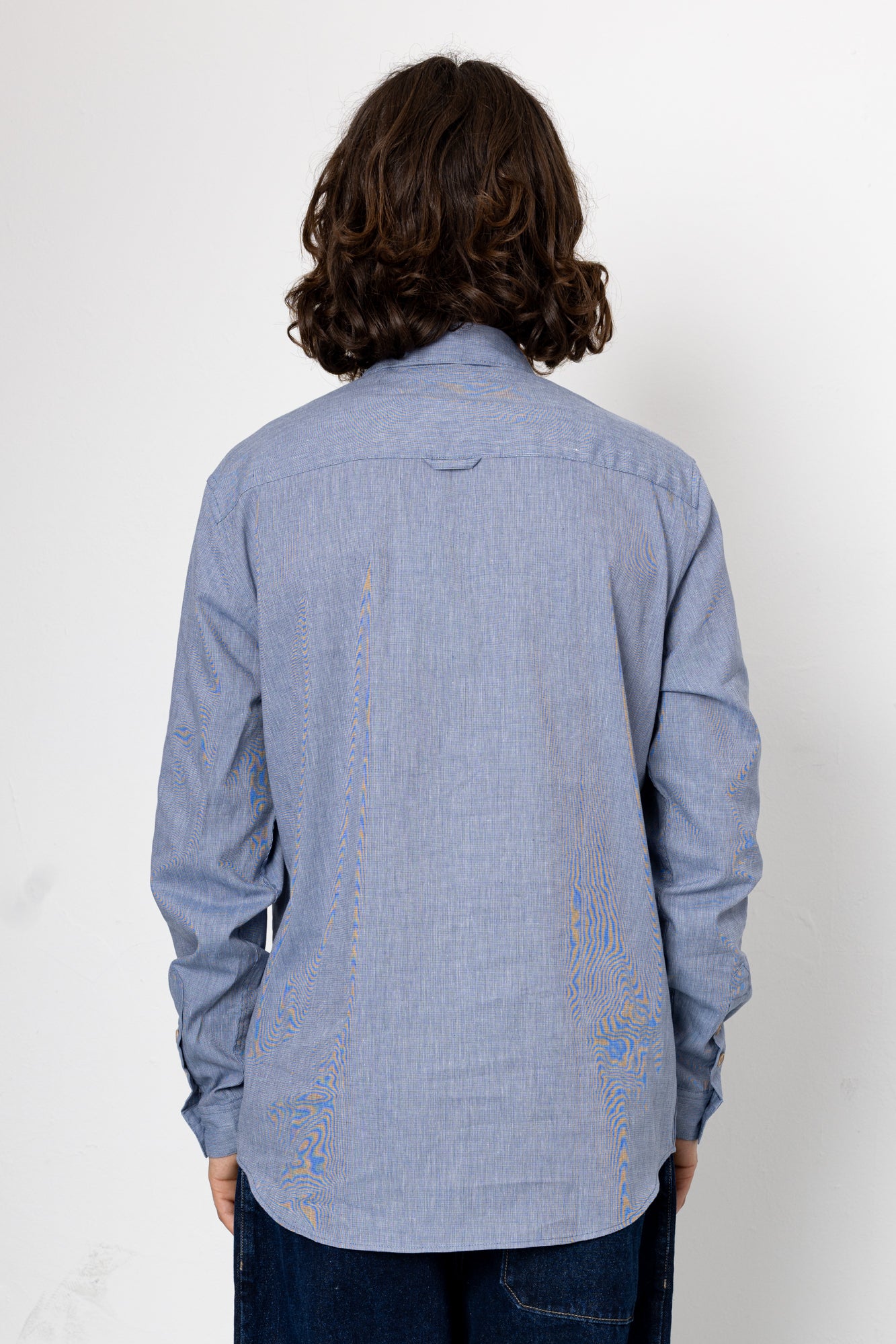 Person wearing a blue denim shirt with a plain white background