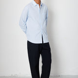 Man wearing a light blue shirt and black pants against a white background