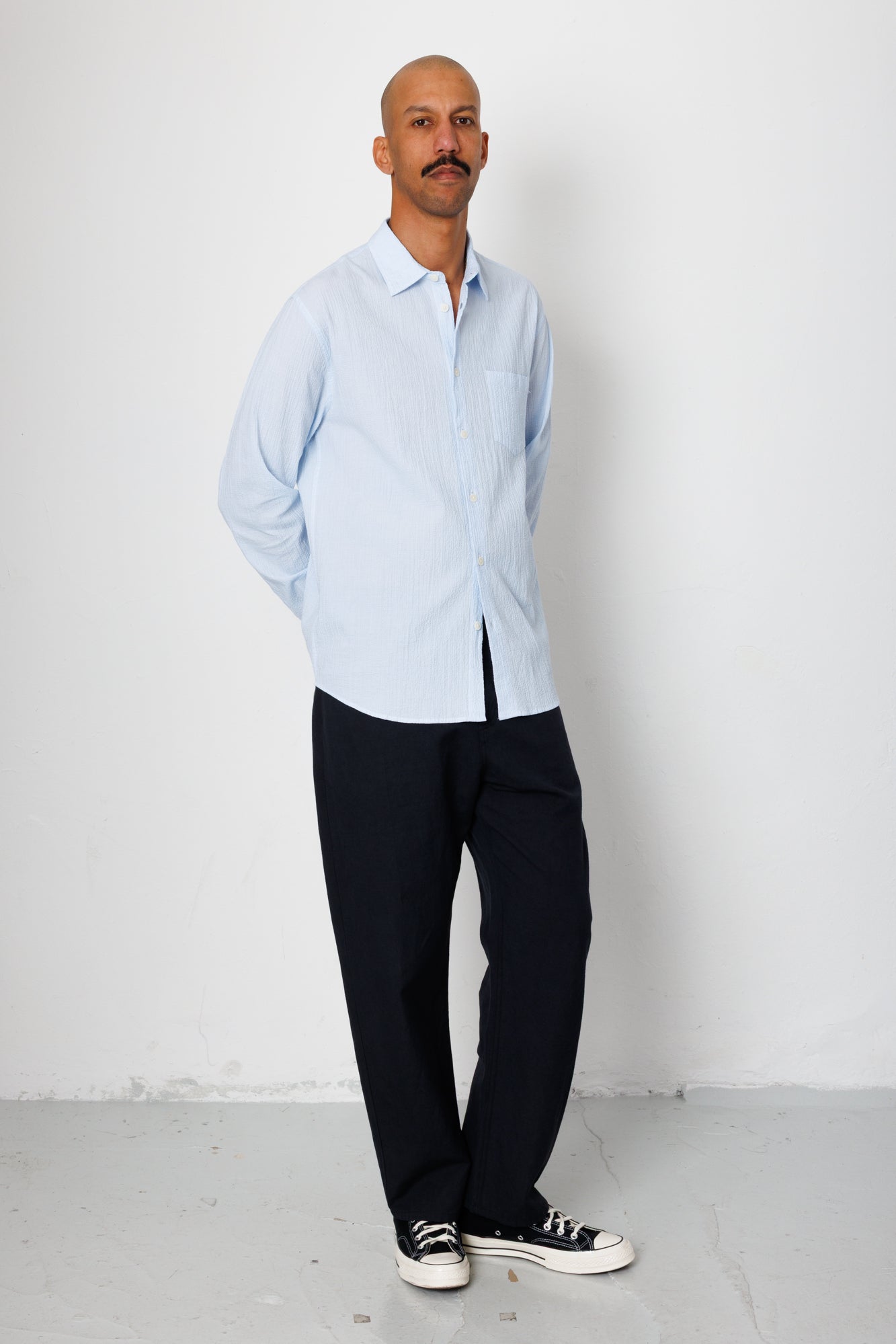 Man wearing a light blue shirt and black pants against a white background