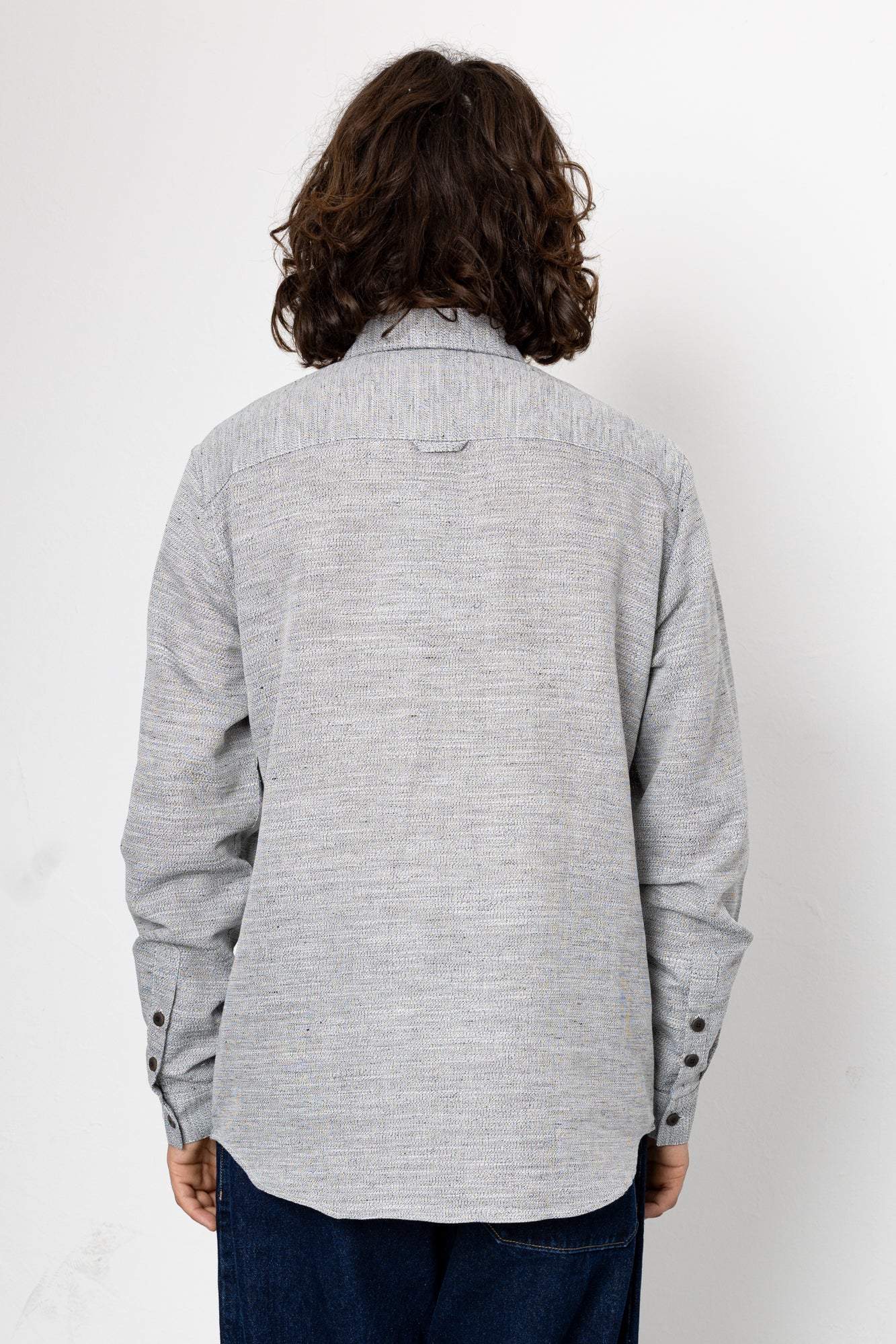 Person wearing a gray textured shirt with long hair on a white background