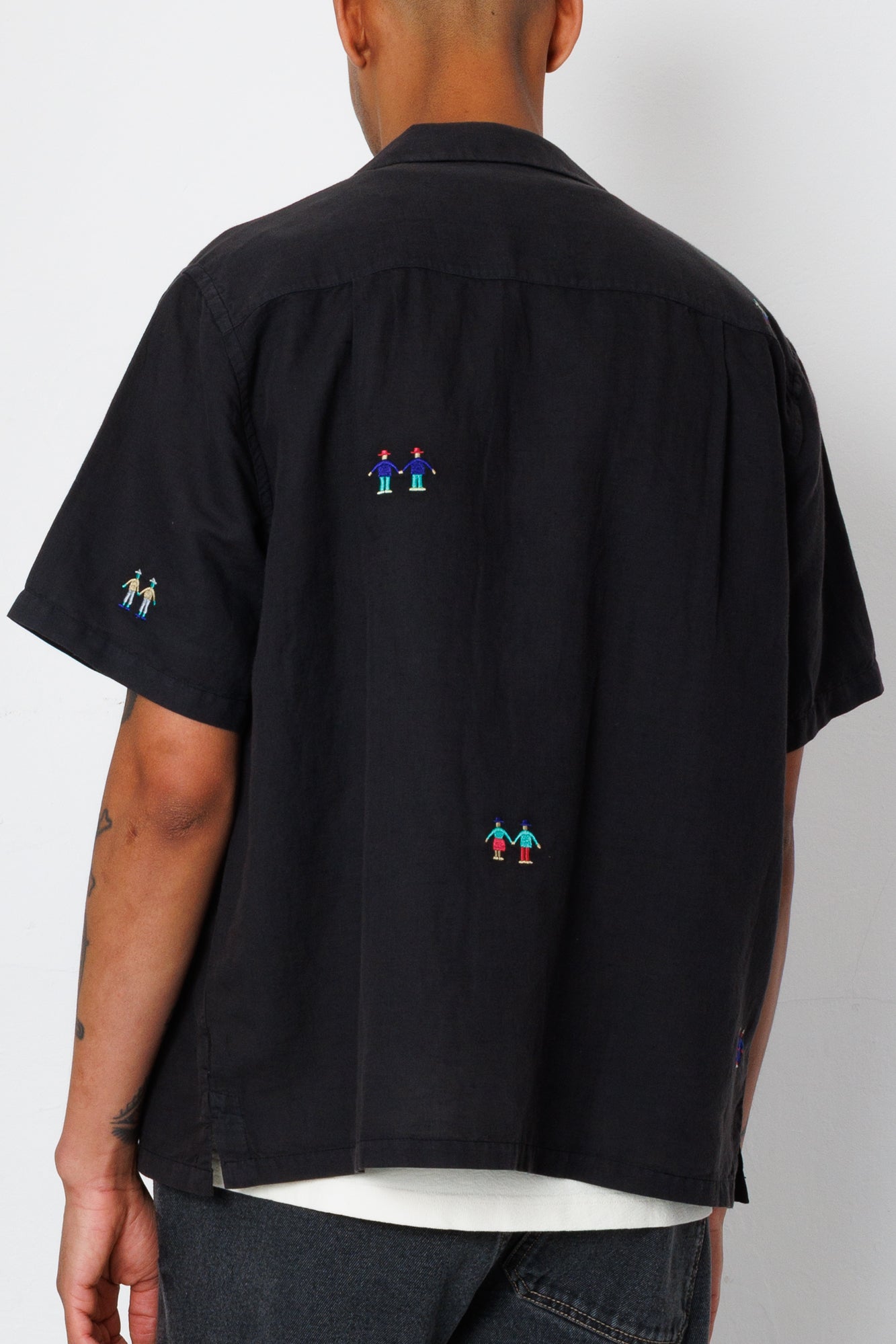Back view of a black shirt with embroidered people detailing.