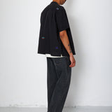 Model facing a white background wearing a black shirt with embroidery. 