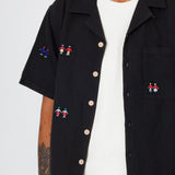Close up of a black shirt with a scattered embroidered people design.