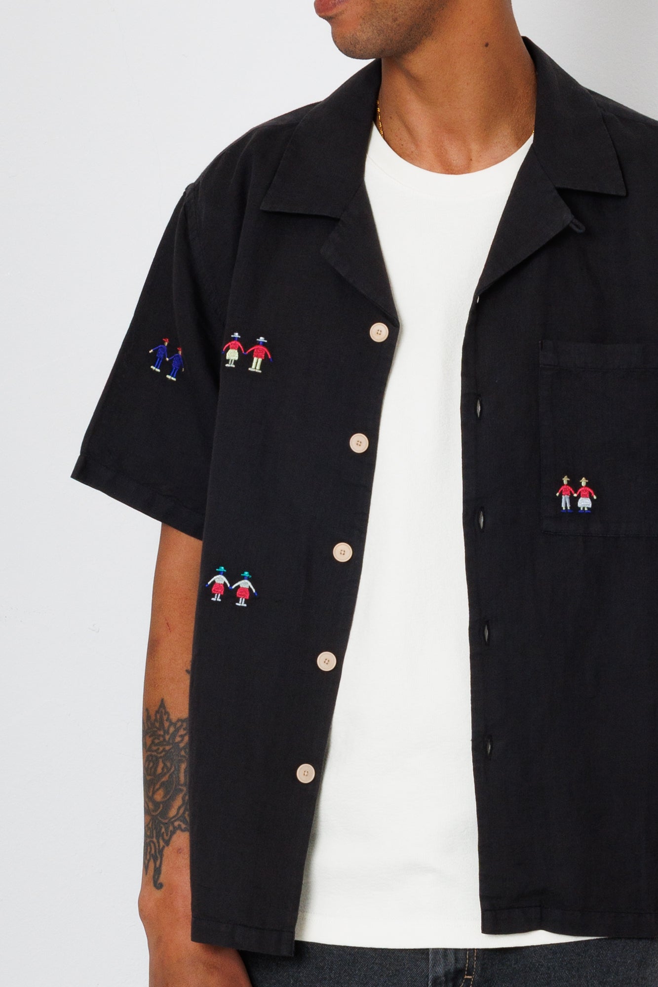 Close up of a black shirt with a scattered embroidered people design.
