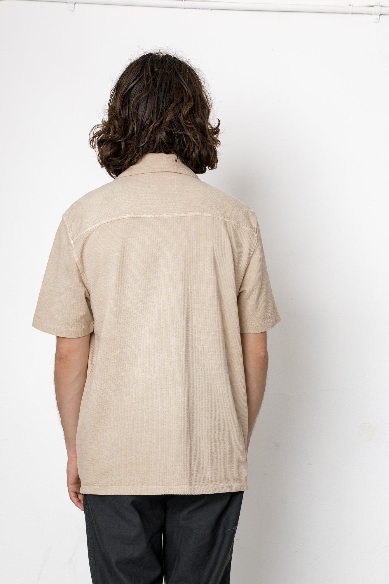 Person wearing a beige short-sleeve shirt against a white background