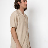 Man wearing a beige short-sleeve shirt against a white background