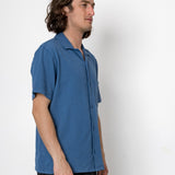 Man wearing a blue shirt standing against a white background