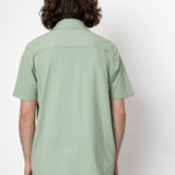 Person wearing a light green shirt and dark pants against a white background