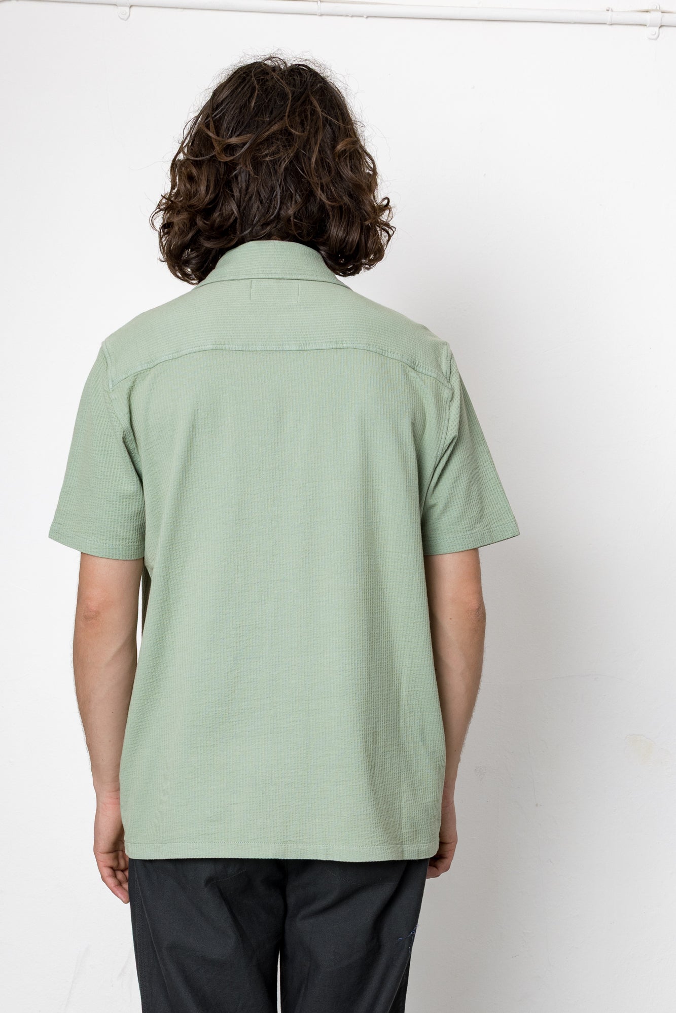 Person wearing a light green shirt and dark pants against a white background