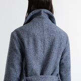 A person shown from the back wearing a textured blue-gray wrap coat with a high collar and waist tie, against a plain white background.