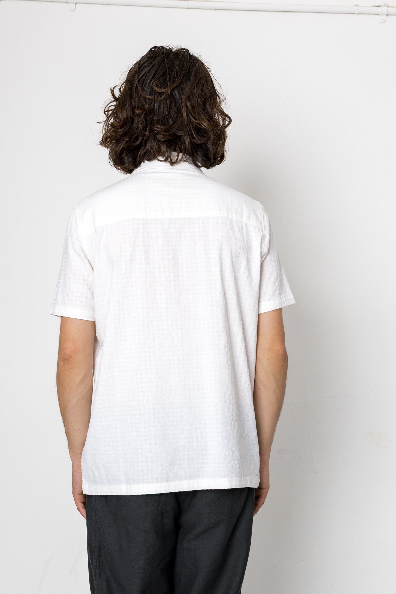 Person wearing a white shirt and black pants against a plain background