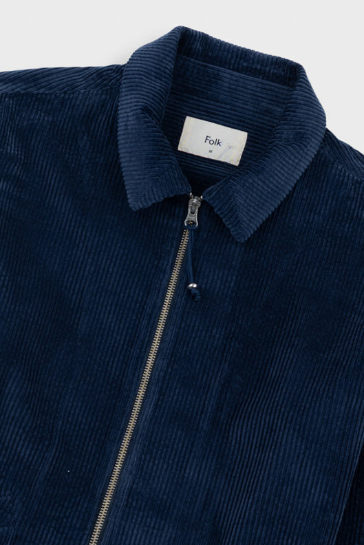 Close-up of a navy blue corduroy zip-up jacket with a collar and a white neck label reading 'Folk'.