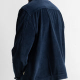 A man wearing a dark navy blue corduroy jacket, shown from a rear three-quarter view against a plain white wall.