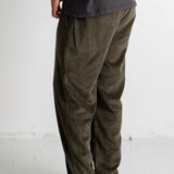 A person shown from the waist down wearing dark olive corduroy pants, a faded black t-shirt, and navy blue canvas sneakers against a white studio wall.
