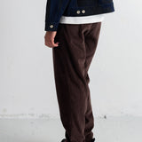 A person shown from the back wearing dark brown corduroy pants, a dark navy jacket, a white undershirt, and black sneakers, standing against a white wall.