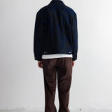 A person shown from the back wearing a dark navy jacket, dark brown pants, a dark navy beanie, and black shoes, standing against a plain white wall.