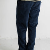 A person shown from the waist down wearing dark navy corduroy pants, a black knit top, and black canvas sneakers with white soles, standing against a white wall.