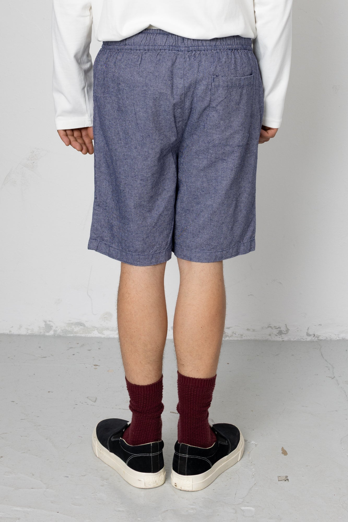 Person wearing blue shorts, white shirt, maroon socks, and black shoes on a plain background