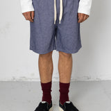 Person wearing blue shorts, white sweater, maroon socks, and black shoes on a plain background