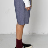 Person wearing blue shorts, white shirt, maroon socks, and black shoes on a plain background