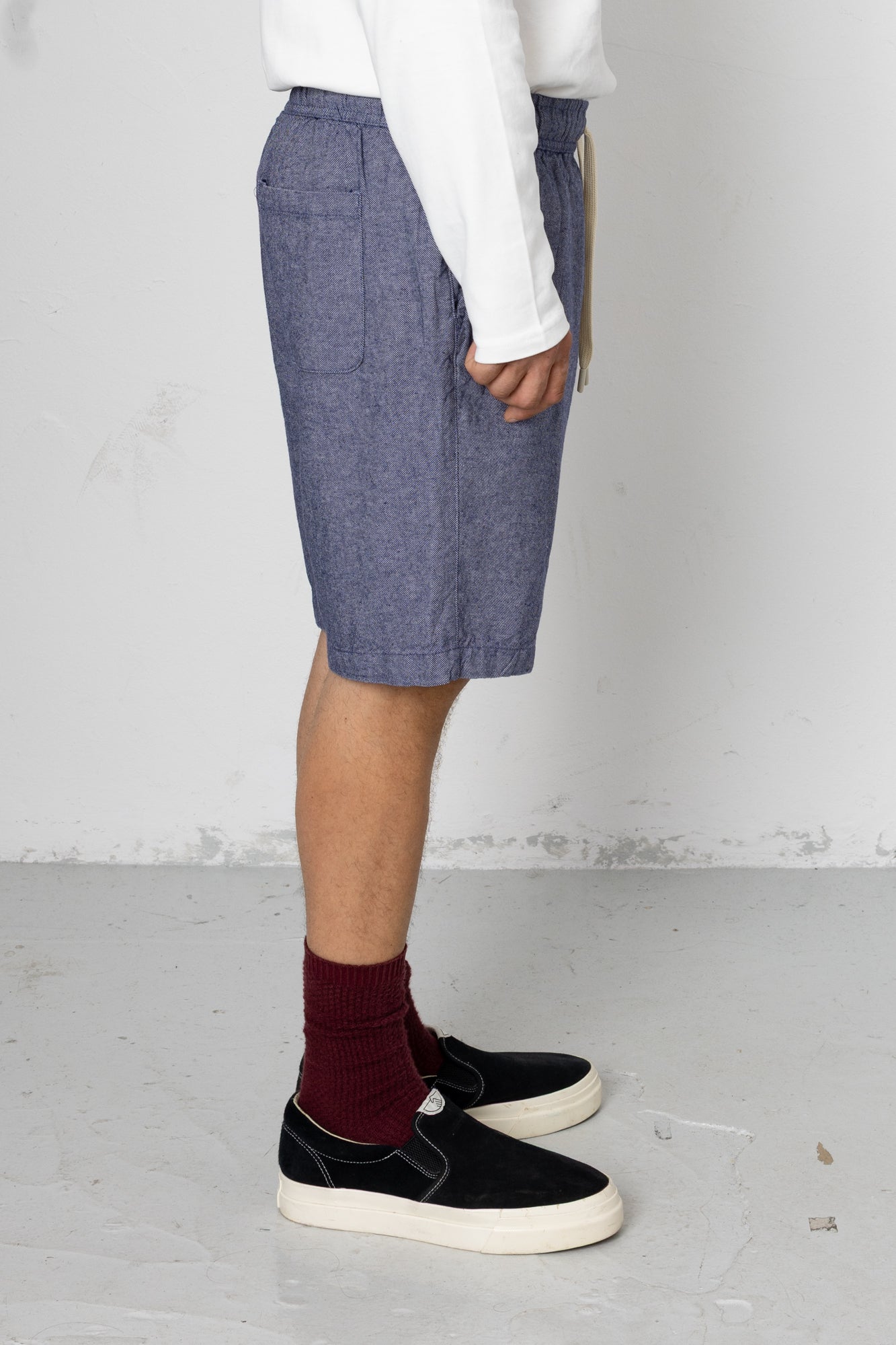 Person wearing blue shorts, white shirt, maroon socks, and black shoes on a plain background