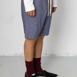 Person wearing blue shorts, white shirt, maroon socks, and black shoes on a light gray floor.