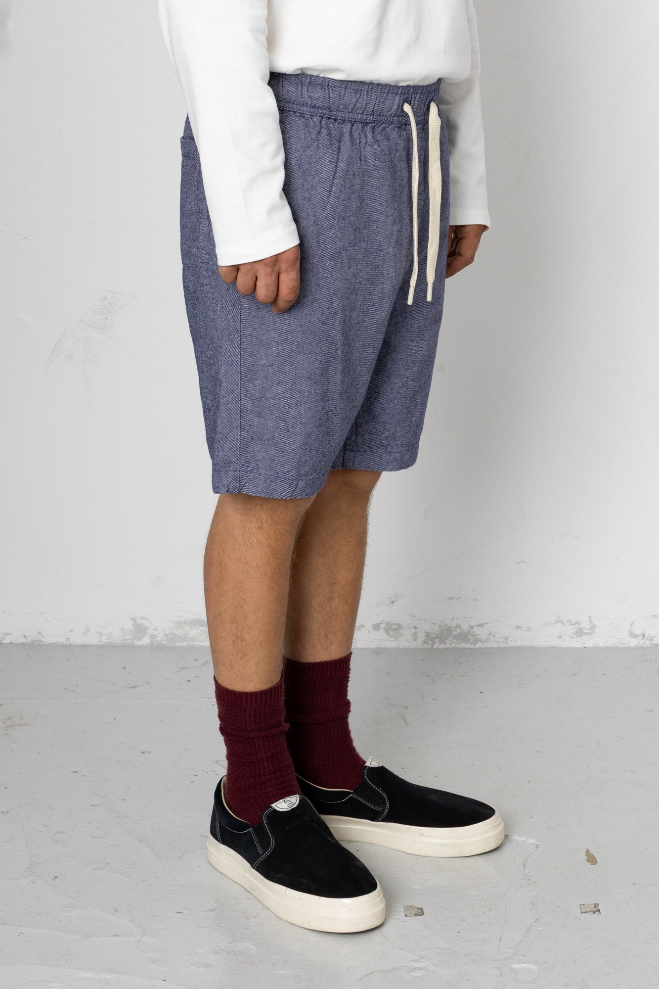 Person wearing blue shorts, white shirt, maroon socks, and black shoes on a light gray floor.