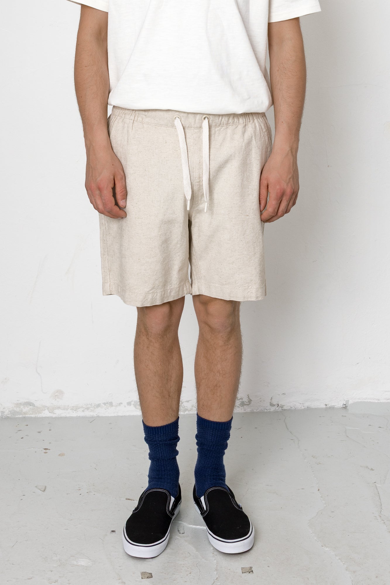 Person wearing beige shorts, white shirt, blue socks, and black shoes on a white background