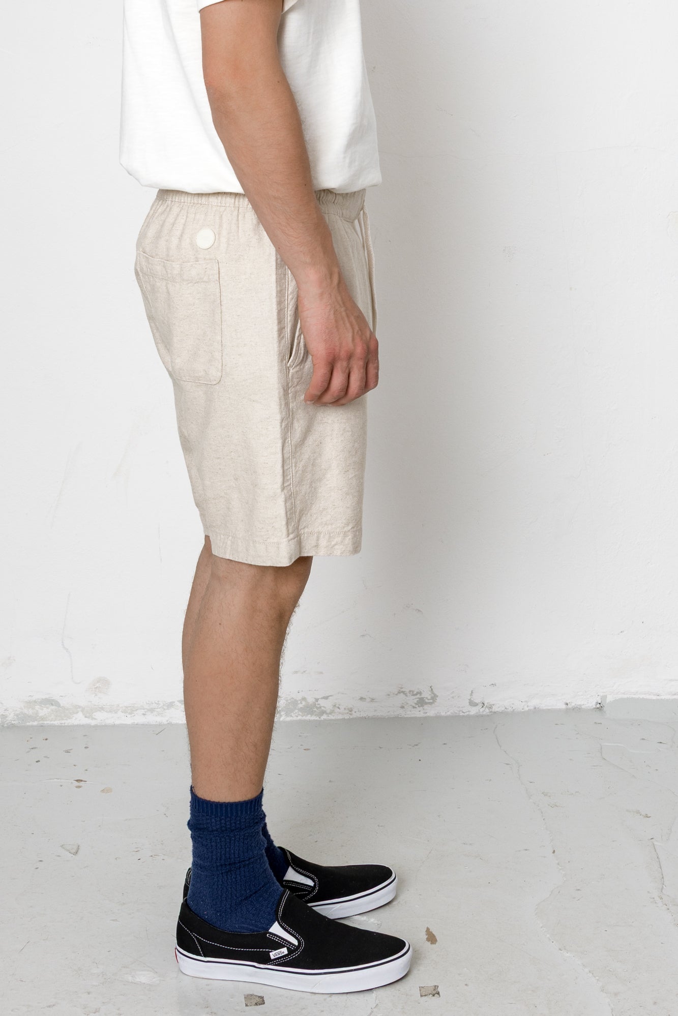 Person wearing beige shorts, black sneakers, and blue socks on a white background