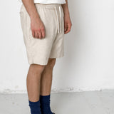 Person wearing beige shorts, white shirt, blue socks, and black shoes on a white background
