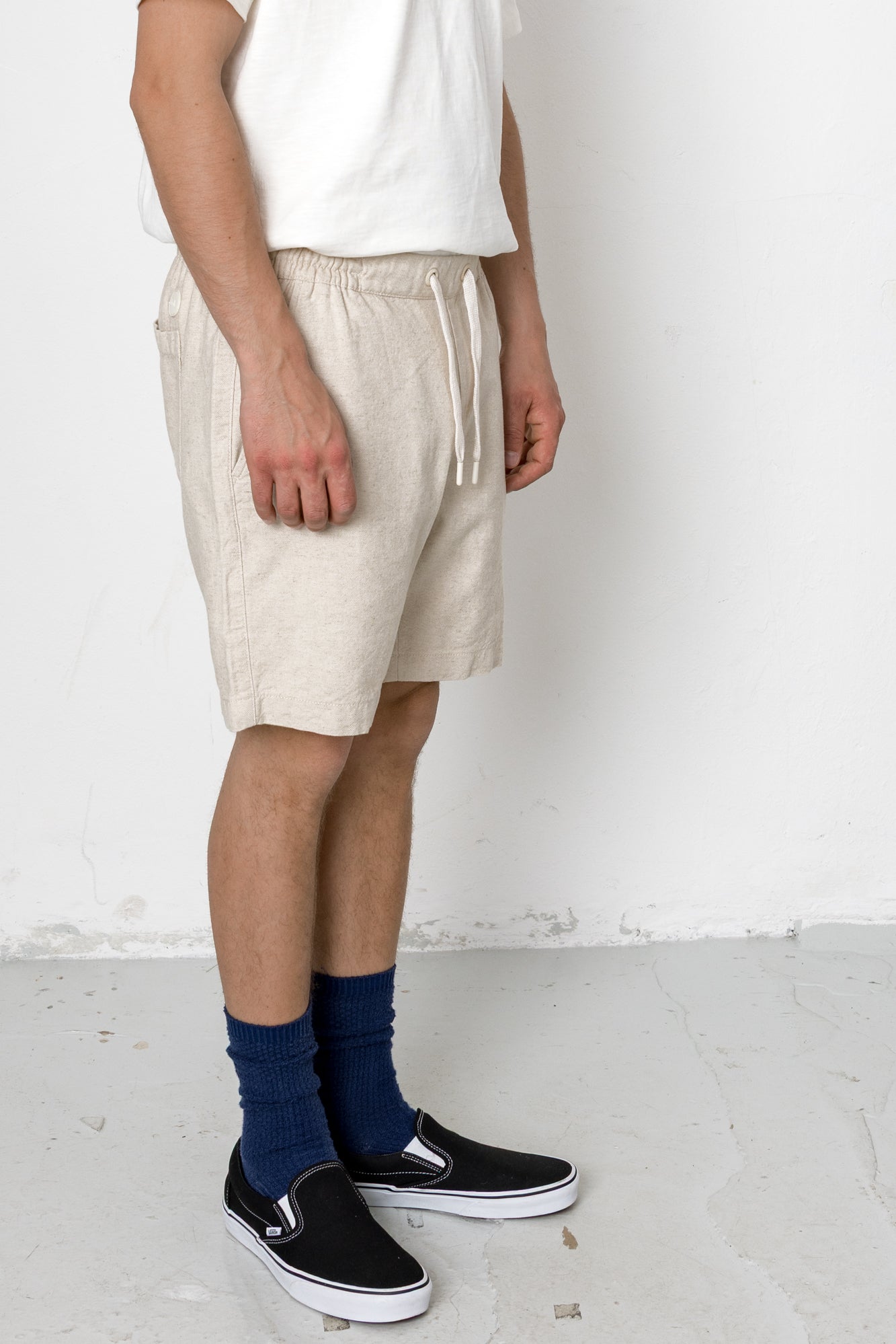 Person wearing beige shorts, white shirt, blue socks, and black shoes on a white background