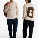 A man and a woman modeling a cream-colored fuzzy knit sweater. The man is shown from the front holding a brown jacket, and the woman is shown from the back featuring a large brown number 8 motif.