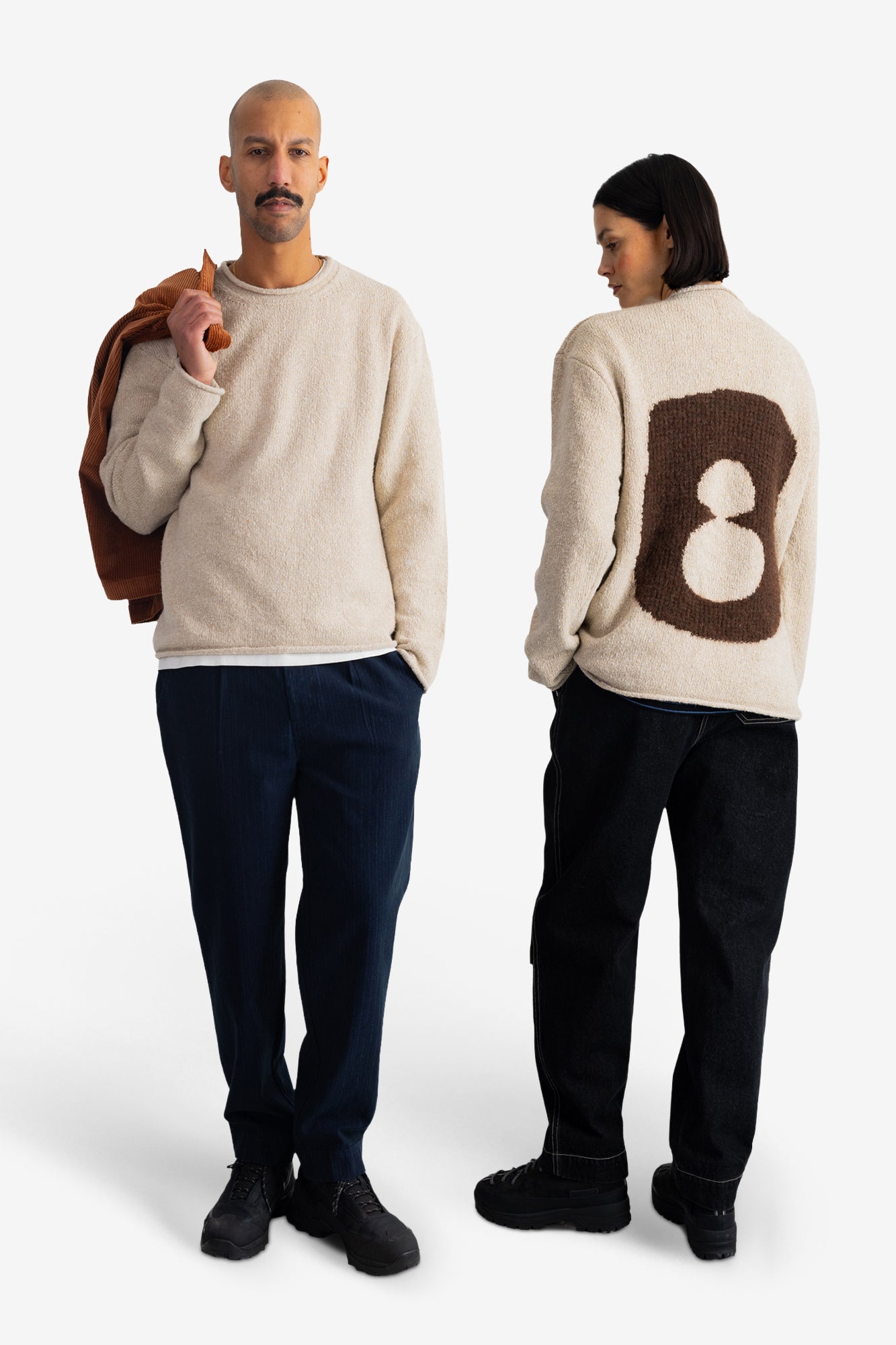 A man and a woman modeling a cream-colored fuzzy knit sweater. The man is shown from the front holding a brown jacket, and the woman is shown from the back featuring a large brown number 8 motif.