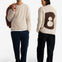 A man and a woman modeling a cream-colored fuzzy knit sweater. The man is shown from the front holding a brown jacket, and the woman is shown from the back featuring a large brown number 8 motif.