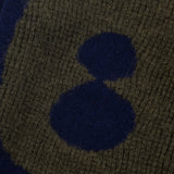 Close-up of a knitted fabric with a dark blue square and two smaller dark blue circles on a green background.