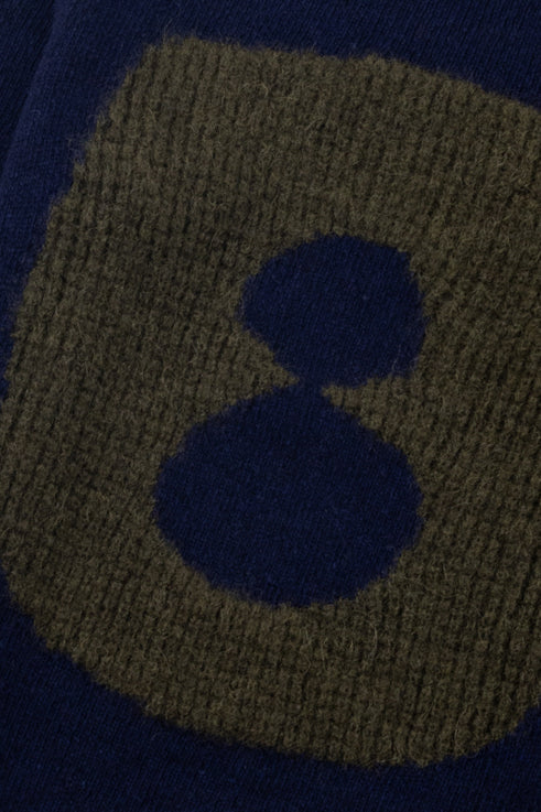 Close-up of a knitted fabric with a dark blue square and two smaller dark blue circles on a green background.