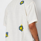 Person wearing a white shirt with colorful designs on the back and arms against a plain background
