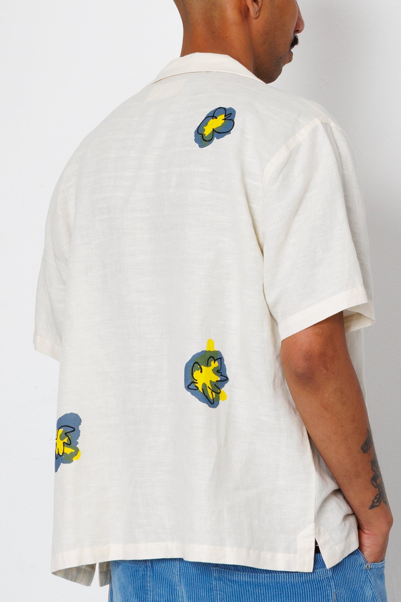 Person wearing a white shirt with colorful designs on the back and arms against a plain background