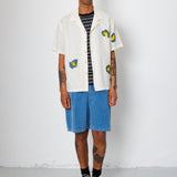 Man wearing a white shirt with colorful designs, blue shorts, and black sneakers against a white background