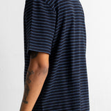 A man wearing a black short-sleeve t-shirt with thin blue horizontal stripes, shown from a side-back angle against a plain white wall.