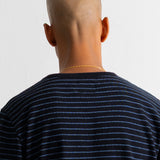 Back view of a bald man wearing a black and blue striped t-shirt, standing against a plain white wall.