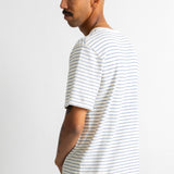 A man wearing a white short-sleeve t-shirt with thin blue horizontal stripes, shown from a side profile against a plain white wall.