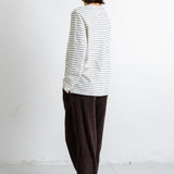 A model shown from the back wearing a white long-sleeve shirt with thin dark horizontal stripes and dark brown wide-leg trousers, standing against a white wall.