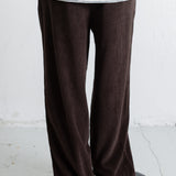 A person shown from the back wearing dark brown wide-leg corduroy pants and a cream striped long-sleeve top, standing against a white wall.